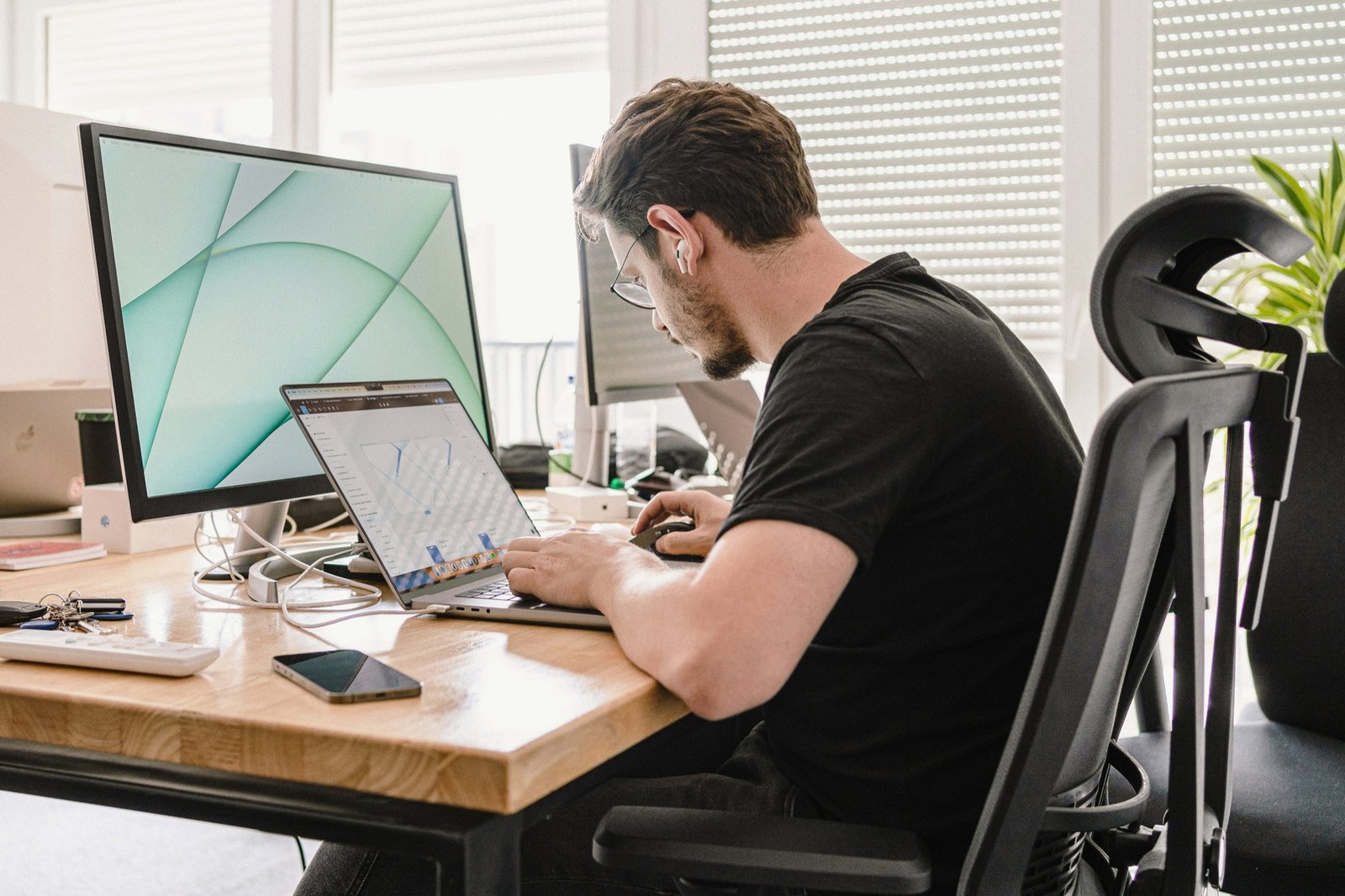 Man working at a laptop in a bright office, one hand on a mouse