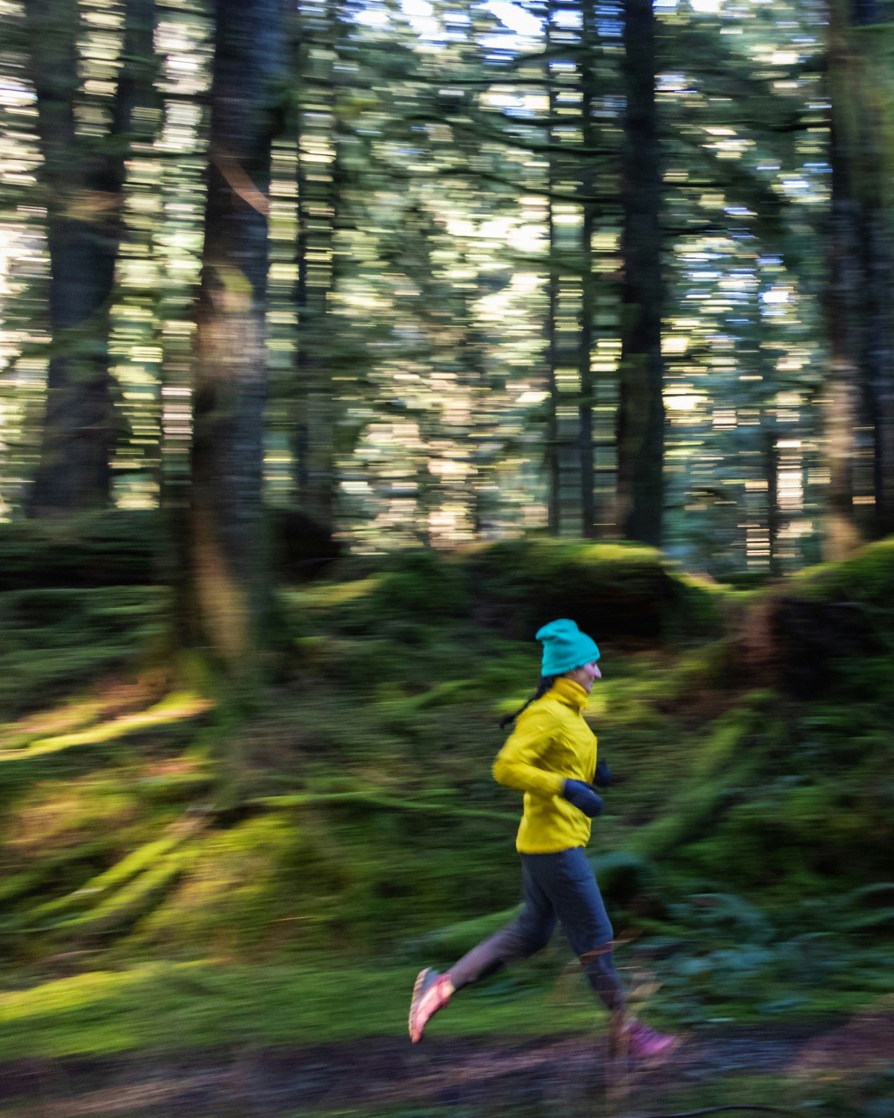 A runner in a yellow jacket and teal hat moving through a forest