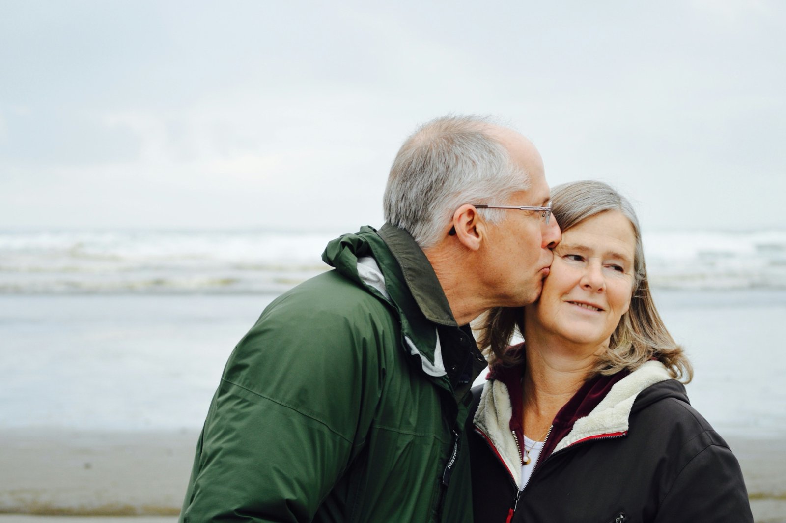 Couple on a beach, one kissing the other's cheek